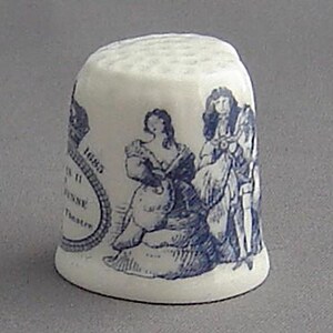 May include: A white ceramic thimble with a blue and white design featuring a scene of three people. The thimble has the text "1685" and "The Theatre Royal Drury Lane" on it.