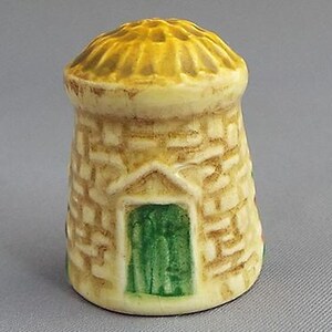 以下が含まれることがあります： 黄色い茅葺き屋根、緑色のドア、茶色のレンガの壁を持つ小さな家の形をしたセラミック製の指ぬきです。