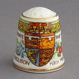 May include: A white ceramic thimble with a colorful design featuring the Royal Coat of Arms and the text "HRH Princess The  Fergusson".