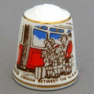 May include: A white porcelain thimble with a red, white, and blue illustration of a London bus with people on board. The text on the thimble reads "Greater London Between the 1st & 6th".