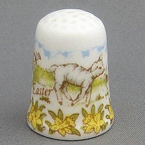 Puede incluir: Dedal de porcelana blanca con un diseño colorido que incluye un cordero, narcisos y la palabra "Easter".