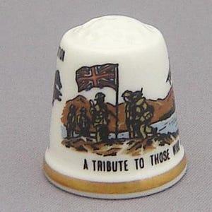 May include: A white ceramic thimble with a gold trim. The thimble features a scene of soldiers marching with a Union Jack flag in the background. The text "A Tribute to Those Who..." is printed on the bottom.