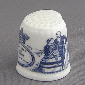 May include: White ceramic thimble with a blue and white design. The design features a royal couple, a crown, and the text "Victoria and Albert Royal Castle 1901".