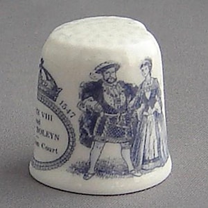 May include: A white ceramic thimble with a blue and white design depicting King Henry VIII and Anne Boleyn. The thimble features the text "H VIII & ANNE BOLEYN - 1547 - The Court".