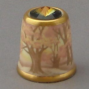 May include: A porcelain thimble with a gold rim and a pink and yellow floral design. The thimble has a clear crystal on top.