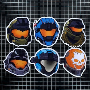 Puede incluir: Seis pegatinas de casco de diferentes colores y diseños. Los cascos son todos de diferentes colores y diseños, incluyendo azul, verde, negro y naranja. Las pegatinas son todas en forma de casco.