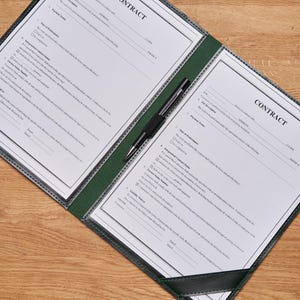 May include: A black and green leather contract folder with a pen. The folder has two pages with the word "CONTRACT" printed at the top of each page.