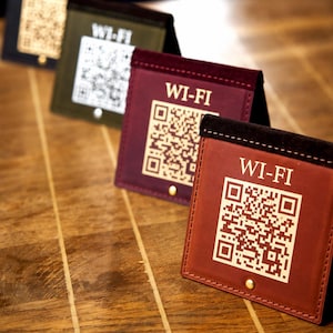 May include: Four square-shaped, tent-style signs made of leather in shades of brown, burgundy, and olive green. Each sign features the text WI-FI at the top and a gold-colored QR code printed below, with a small gold metal stud at the bottom center.