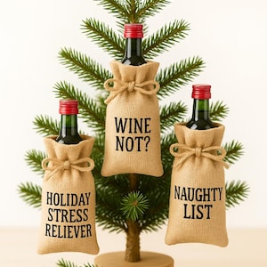 May include: A miniature Christmas tree with three small wine bottles. Each bottle is in a burlap sack with a bow and a different phrase: "Wine Not?", "Holiday Stress Reliever", and "Naughty List". Red berries and greenery are at the base.