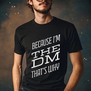 May include: A black t-shirt with white text that reads "Because I'm The DM That's Why".