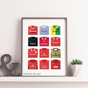 May include: A framed print featuring a collection of twelve soccer jerseys in various colors, including red, blue, and yellow. Each jersey displays sponsor logos such as "SHARP" and "Vodafone". The phrase "FRAME NOT INCLUDED" is printed at the bottom.