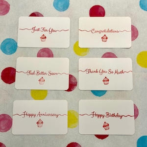 May include: Six rectangular white gift tags with rounded corners, each featuring red text and a small red cupcake illustration. The phrases include Just For You, Congratulations, Feel Better Soon, Thank You So Much, Happy Anniversary, and Happy Birthday.