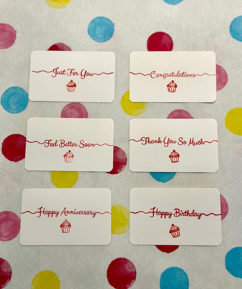 May include: Six rectangular white gift tags with rounded corners, each featuring red text and a small red cupcake illustration. The phrases include Just For You, Congratulations, Feel Better Soon, Thank You So Much, Happy Anniversary, and Happy Birthday.