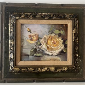 May include: Oil painting of yellow roses in a square frame. The artwork features a close-up of two roses with green leaves and a bud. The frame is dark green with gold accents, adding a vintage aesthetic.