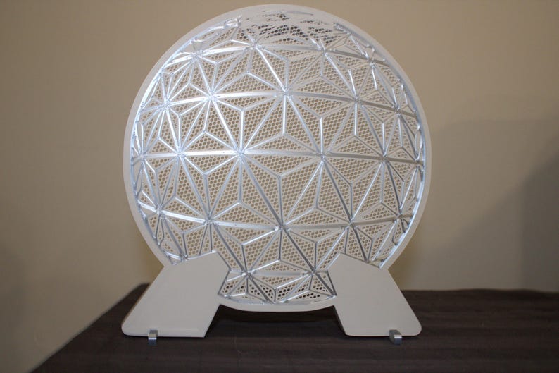 May include: A decorative, geometric, silver-colored sphere with a complex star-like pattern. The sphere is supported by two white, rectangular feet. The design is modern and intricate, suitable for home decor.