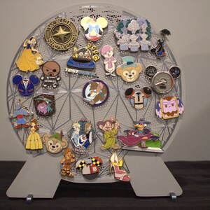May include: A gray, spherical pin display stand filled with colorful Disney character pins. The pins feature characters like Snow White, Mickey Mouse, and Duffy Bear. The stand is supported by two gray feet.