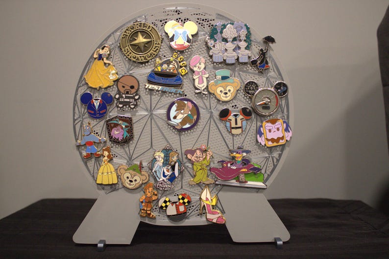 May include: A gray, spherical pin display stand filled with colorful Disney character pins. The pins feature characters like Snow White, Mickey Mouse, and Duffy Bear. The stand is supported by two gray feet.