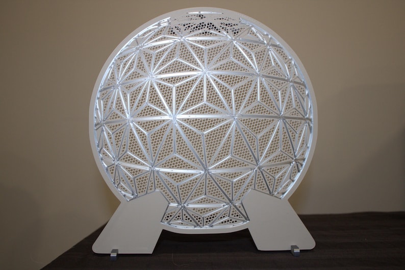 May include: A white, geometric, decorative object with a spherical shape. The design features a repeating pattern of interconnected triangles and star shapes. It stands on two white, rectangular supports.