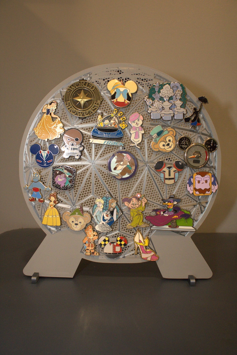 May include: A gray, geometric pin display stand holding a collection of Disney character pins. The pins feature characters like Mickey Mouse, Snow White, and others. The stand is on a gray surface.