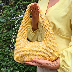 May include: A yellow and white crochet handbag with a curved handle. The bag is held by a person wearing a yellow blouse. The words "Crochet Pattern" are written on the side of the bag.