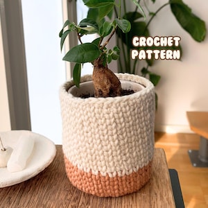 Pode incluir: Um vaso de planta de crochê com a parte superior branca e a inferior marrom claro. O vaso está cheio de terra e uma pequena planta com folhas verdes. O texto "CROCHET PATTERN" é visível na imagem.