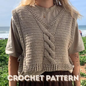 May include: A beige crochet vest with a V-neck and a cable knit design. The vest is worn over a light brown t-shirt. The text "CROCHET PATTERN" is displayed in white letters at the bottom of the image. The background shows a beach scene.