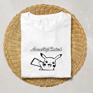May include: White t-shirt with a black graphic of a cartoon character giving the middle finger. The text "Locally Hated" is above the character. The shirt is folded on a woven, circular surface.