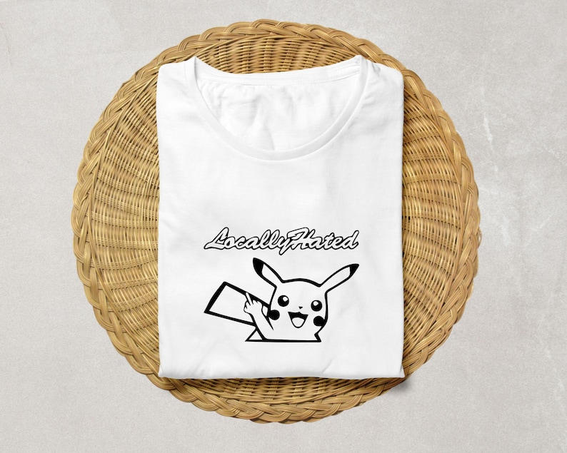 May include: White t-shirt with a black graphic of a cartoon character giving the middle finger. The text "Locally Hated" is above the character. The shirt is folded on a woven, circular surface.