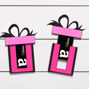 May include: Two pink gift boxes with black bows and a black and yellow Amazon gift card inside one of the boxes.