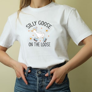 May include: White t-shirt with a cartoon goose on roller skates and the words "Silly Goose on the Loose." The design includes daisies and stars. The shirt is made of a soft, comfortable material.