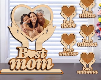 May include: Wooden cutout of a heart with hands holding it up, with a photo frame in the center. The cutout has the text "Best Mom" with a small heart in the word "Best". There are six additional cutouts of hearts with hands holding them up, each with the text "Best" and a different word in a different language, including "mum", "mere", "mama", "mutter", and "mamma".