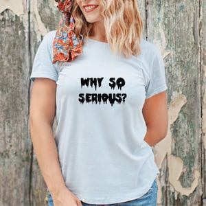 May include: Light blue t-shirt with the phrase "WHY SO SERIOUS?" in black, dripping font. The shirt is made of a soft material and is suitable for casual wear. The model is wearing blue jeans.