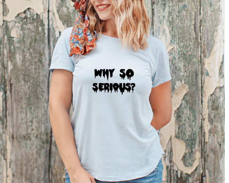 May include: Light blue t-shirt with the phrase "WHY SO SERIOUS?" in black, dripping font. The shirt is made of a soft material and is suitable for casual wear. The model is wearing blue jeans.