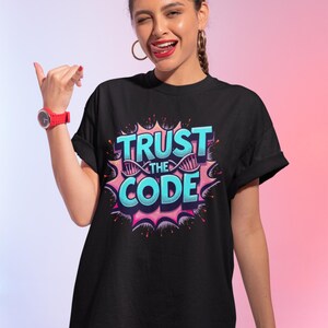 May include: Black t-shirt with the text "TRUST THE CODE" in a comic book style design. The design features blue and pink colours with a DNA strand graphic. The shirt has short sleeves.