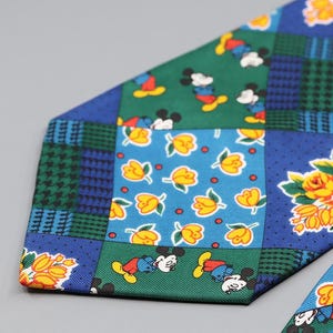 May include: A colorful necktie with a patchwork design featuring Mickey Mouse, yellow flowers, and floral patterns. The tie has a mix of blue, green, and yellow squares with a houndstooth pattern.