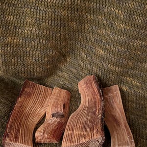 Può includere: Tre pezzi di legno grezzo, probabilmente cedro, di colore marrone rossiccio naturale e di consistenza granulosa. Il legno è disposto su un tessuto a maglia verde.