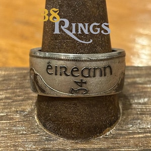 May include: A silver coin ring with the inscription "éireann" and the number "34" on it. The ring is on a wooden display stand.
