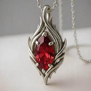 Peut inclure: Collier pendentif argenté orné d'une pierre précieuse rouge vif taillée en marquise. Le pendentif présente un motif de flamme stylisé avec des détails complexes. La chaîne du collier est également argentée, créant un bijou élégant.