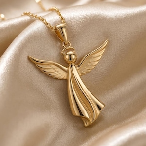 A beautifully sculpted angel pendant, available in both radiant gold and warm rose gold finishes, hangs from a delicate chain, resting on a soft, light-colored draped fabric, showcasing its intricate details, outstretched wings, halo, and flowing gown, embodying a serene guardian angel design.