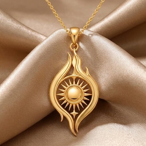 May include: A gold pendant necklace with a sunburst design within a flame-like shape. The pendant hangs from a delicate chain, creating a striking jewelry piece. The necklace is displayed on a satin fabric.