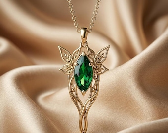 May include: A gold pendant necklace featuring a marquise-cut emerald green gemstone at the center. The metal setting is shaped like delicate leaves and swirling vines, suspended from a thin gold chain with small, uniform circular links.