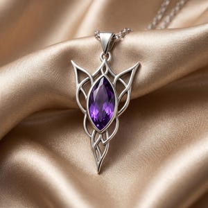 A close-up of an ornate Elven Birthstone Pendant Necklace, featuring a vibrant marquise-cut purple amethyst gemstone at its center. The intricate metalwork, available in both polished gold-tone and silver-tone finishes, forms a symmetrical, flowing design reminiscent of fantasy or Celtic art. The pendant hangs from a delicate cable chain, showcasing its detailed craftsmanship and mystical theme against a neutral background.