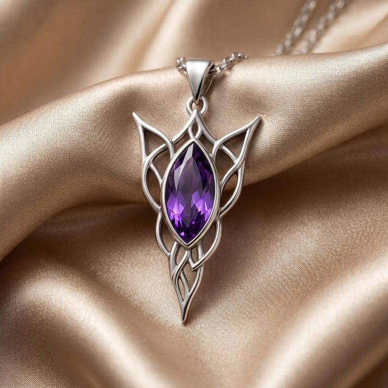 A close-up of an ornate Elven Birthstone Pendant Necklace, featuring a vibrant marquise-cut purple amethyst gemstone at its center. The intricate metalwork, available in both polished gold-tone and silver-tone finishes, forms a symmetrical, flowing design reminiscent of fantasy or Celtic art. The pendant hangs from a delicate cable chain, showcasing its detailed craftsmanship and mystical theme against a neutral background.