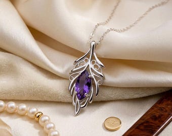 May include: A silver pendant necklace featuring a marquise-cut purple gemstone set within a delicate, openwork leaf-shaped frame. The pendant hangs from a thin silver chain, accompanied by a strand of white pearls and a small gold circular charm.