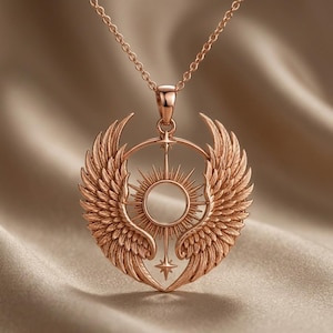 K&ouml;nnte beinhalten: Eine Halskette mit Anh&auml;nger aus Ros&eacute;gold, die ein detailliertes Design aus Fl&uuml;geln, einem Sonnenstrahl und einem Stern aufweist. Der Anh&auml;nger h&auml;ngt an einer zarten Kette. Die Halskette wird vor einem neutralen Hintergrund gezeigt.