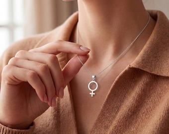 May include: A silver-toned necklace featuring a pendant shaped like the female gender symbol. The pendant is suspended from a delicate, thin silver chain that rests against the collarbone. The design is simple, polished, and metallic.