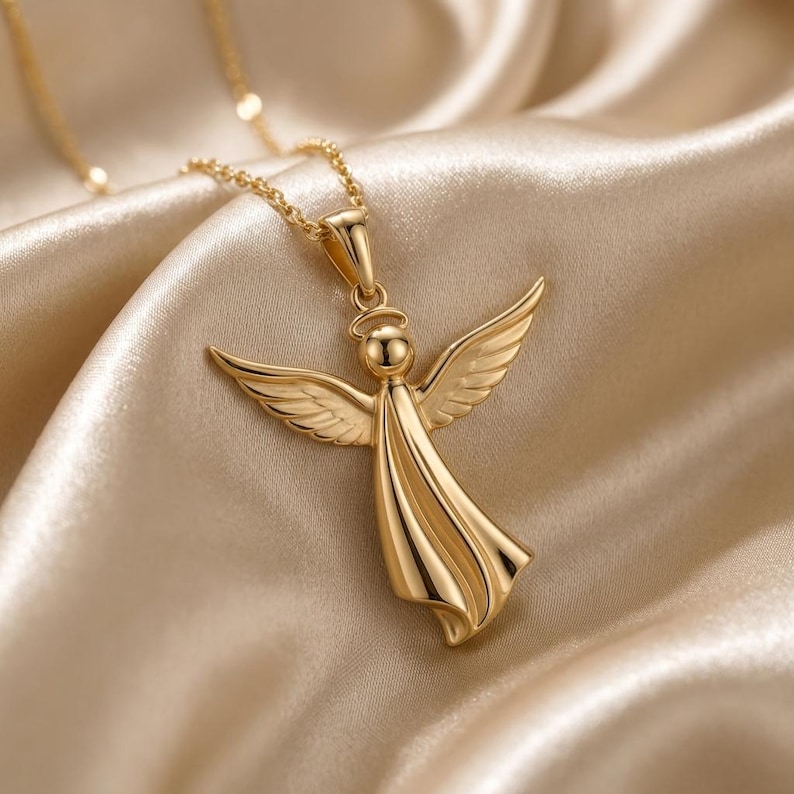 A beautifully sculpted angel pendant, available in both radiant gold and warm rose gold finishes, hangs from a delicate chain, resting on a soft, light-colored draped fabric, showcasing its intricate details, outstretched wings, halo, and flowing gown, embodying a serene guardian angel design.