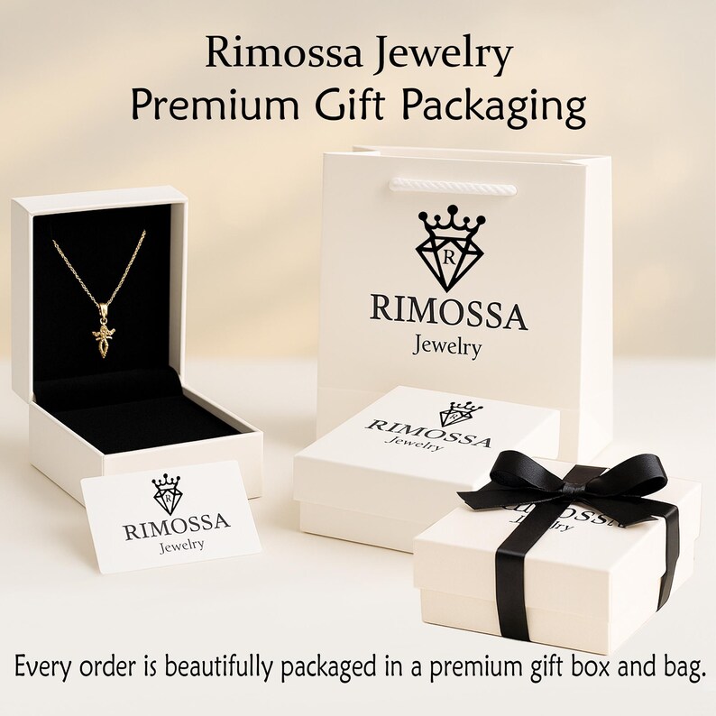 Pode incluir: Um colar com pingente dourado &eacute; exibido em uma caixa de joias branca aberta. Uma sacola de presente branca e duas caixas brancas, todas com o logotipo "Rimossa Jewelry", tamb&eacute;m est&atilde;o presentes. Uma caixa &eacute; adornada com uma fita preta. O texto diz "Rimossa Jewelry Premium Gift Packaging."
