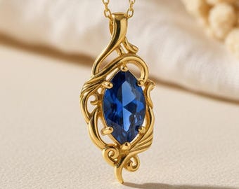 May include: A gold-toned pendant necklace featuring a central marquise-cut deep blue gemstone. The metal setting displays intricate, swirling, vine-like filigree patterns that frame the stone. The pendant hangs from a delicate gold-toned chain.