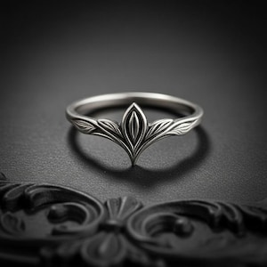 May include: A silver-toned metal ring featuring a central pointed design with engraved leaf-like patterns extending along the band. The ring has a polished finish with darkened recessed areas that highlight the intricate botanical-inspired detailing.